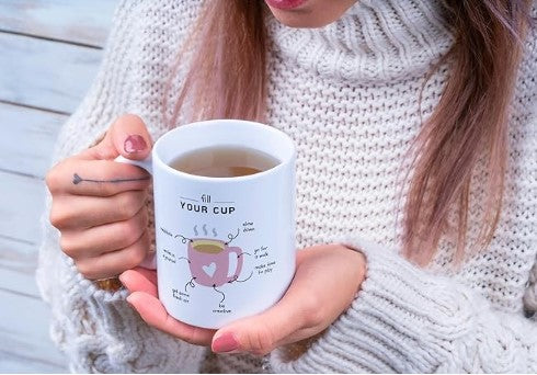 Person holding a mug with inspirational design on it, wearing a white sweater.