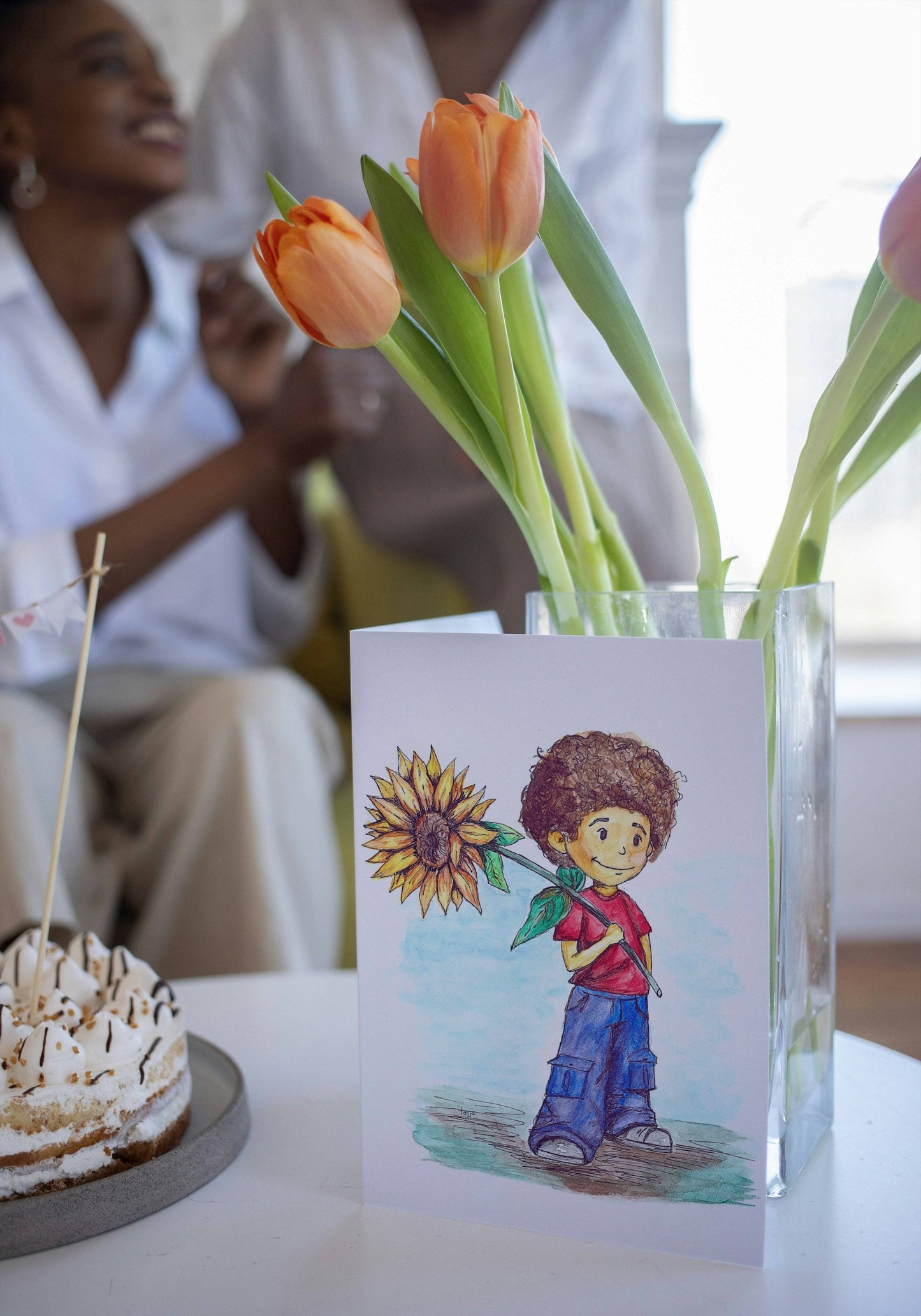 Sunflower Boy Greeting Card - Hand Painted | Watercolor Print featuring a curly-haired boy holding a sunflower, displayed beside tulips and cake.